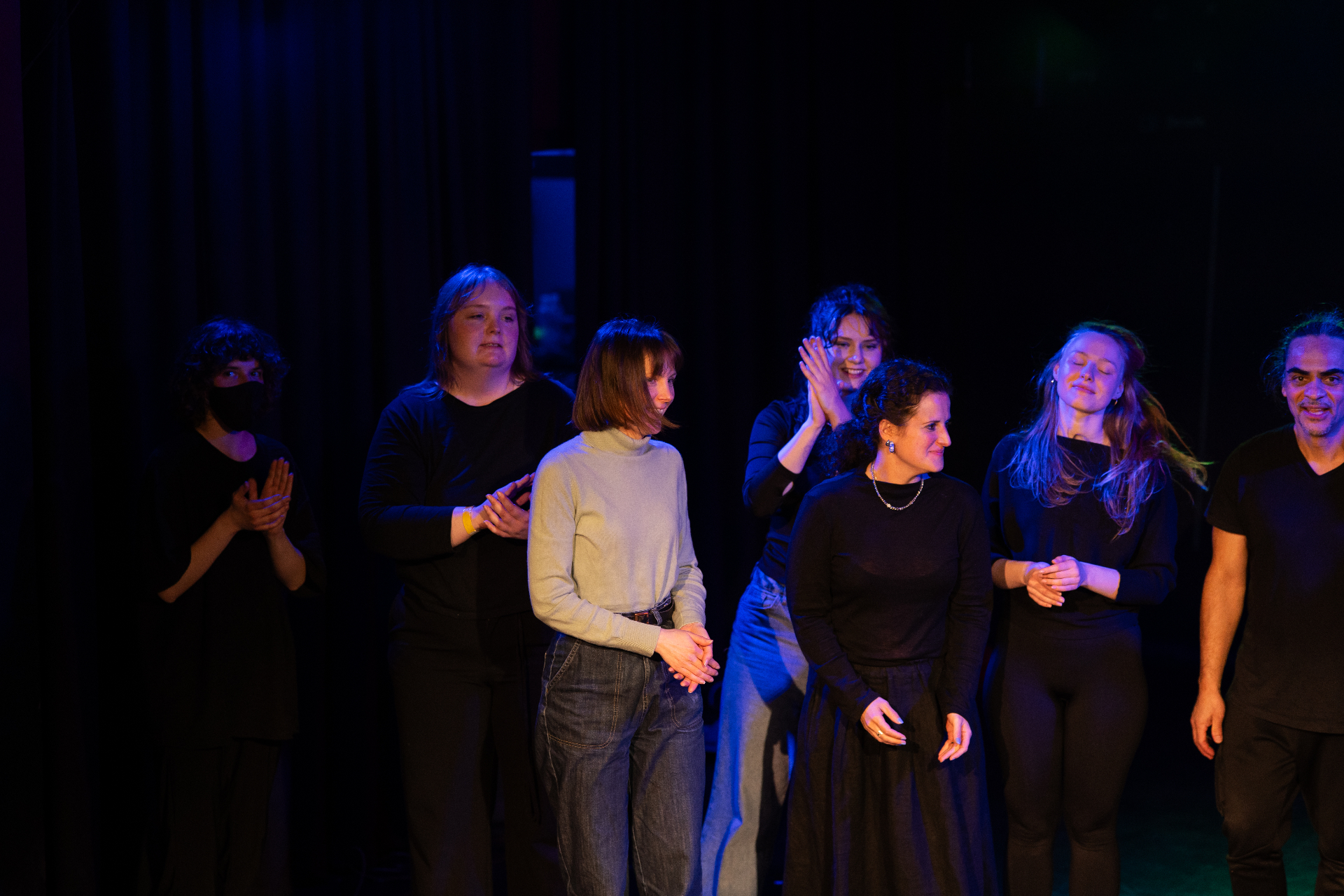 Performers standing together on stage bathed in blue light