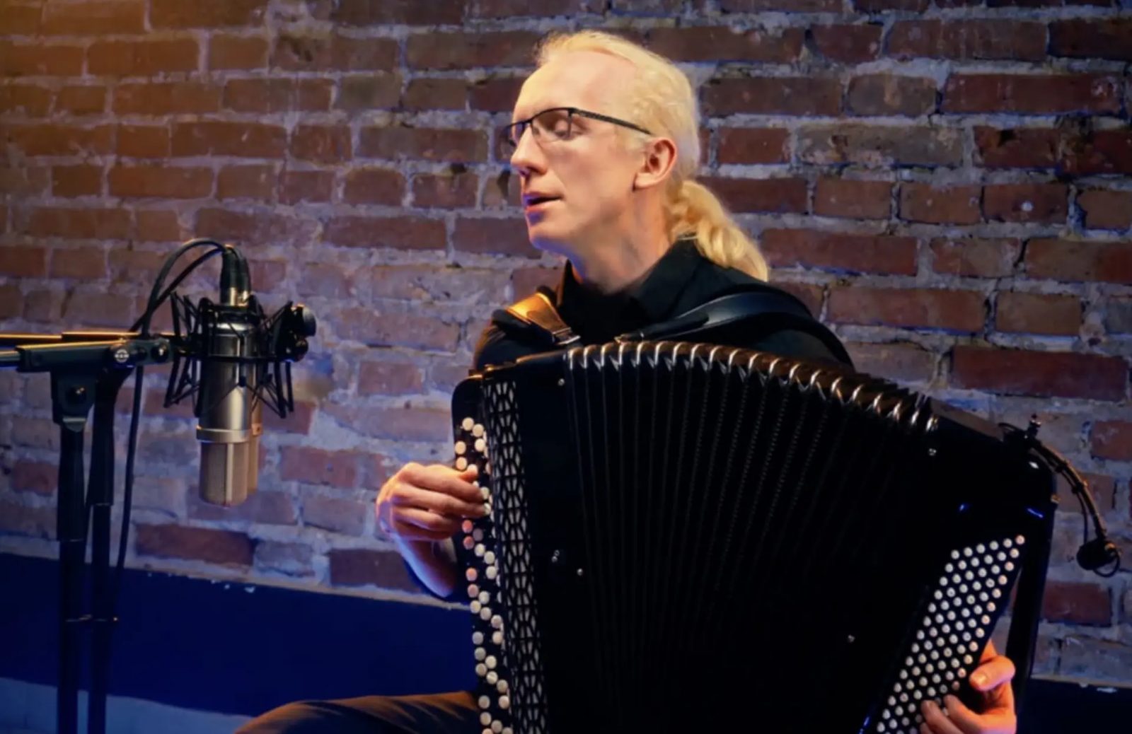 Accordionist performing a live session against a brick wall