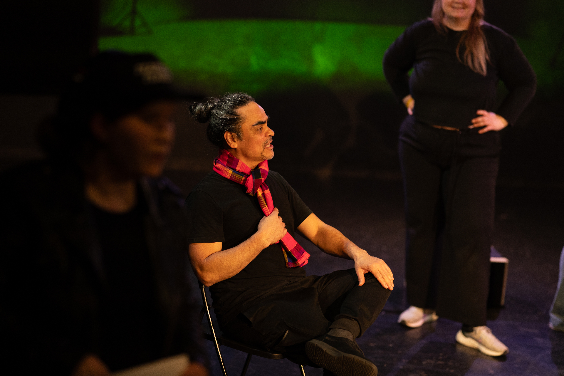 Performer seated on stage wearing a red-and-black scarf