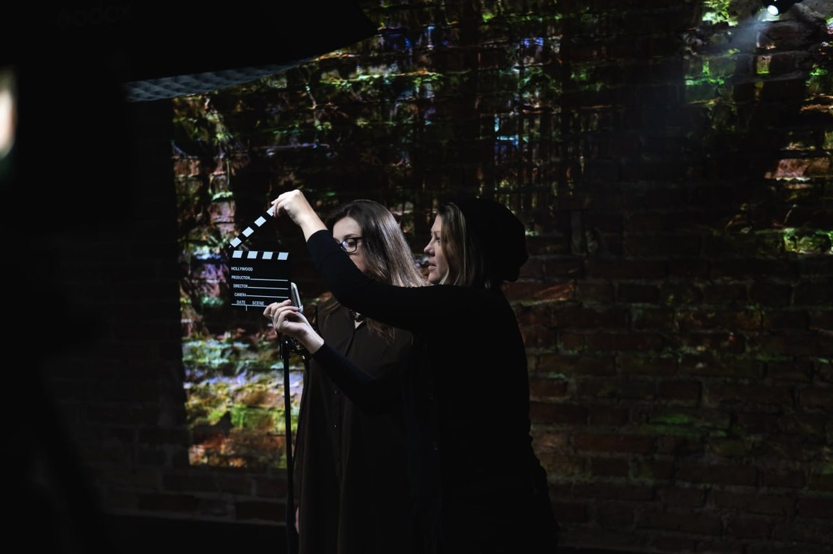 Filmmaker holding a clapperboard before a projected brick wall scene