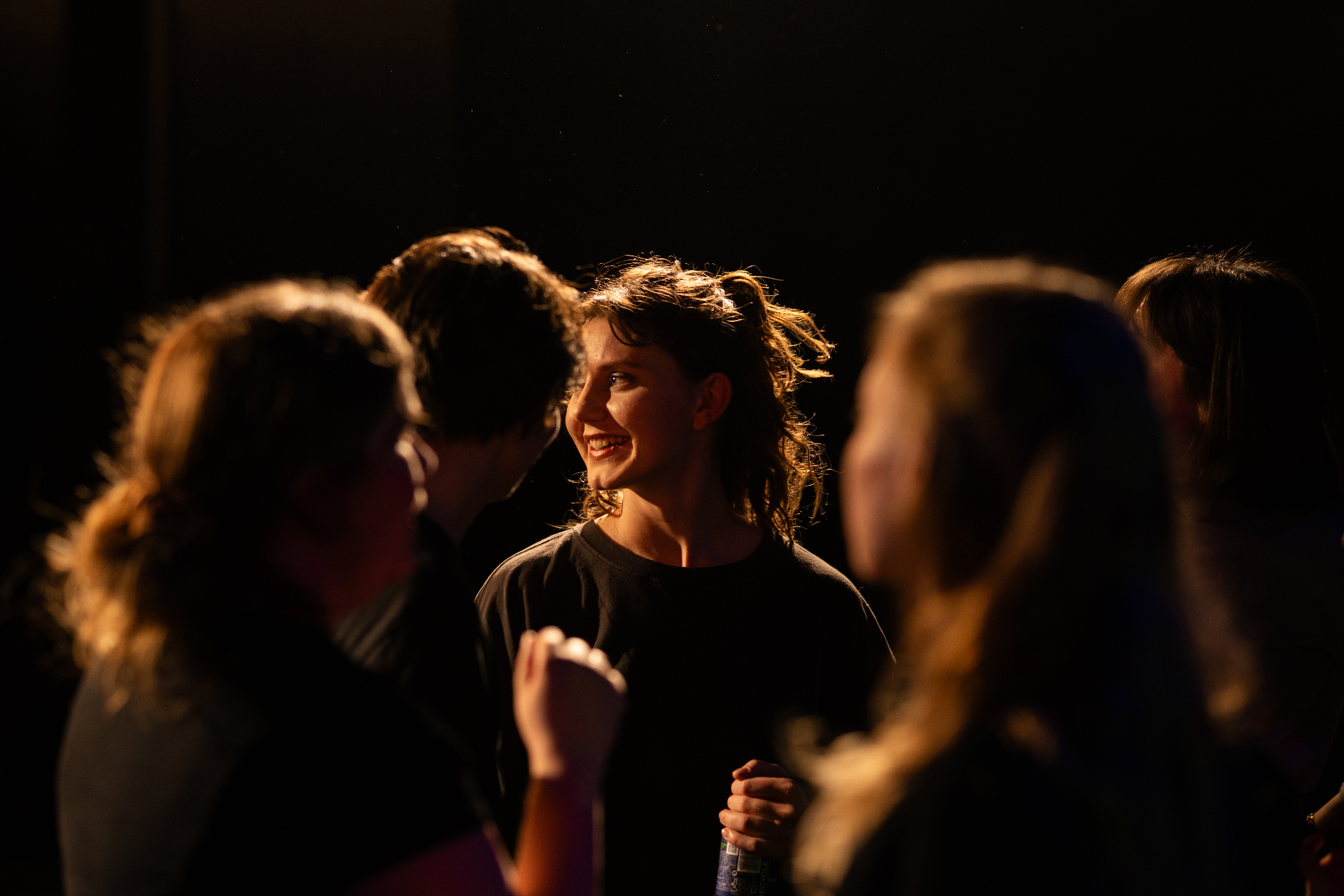 Smiling performer in warm stage light surrounded by the ensemble