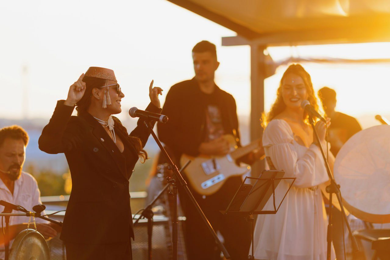Band performing at sunset with singers and musicians on a rooftop stage
