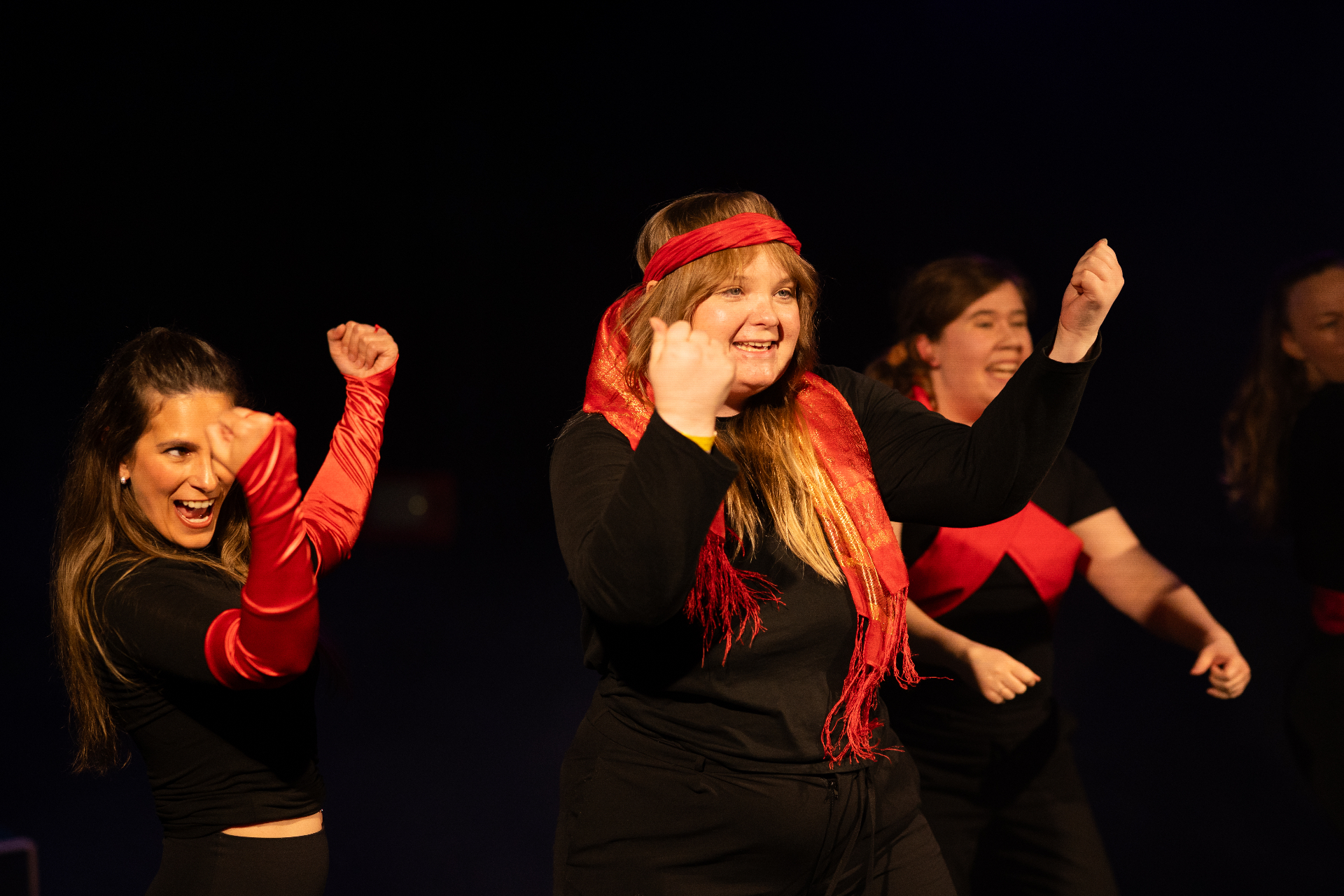 Performers dancing joyfully on stage with red scarves