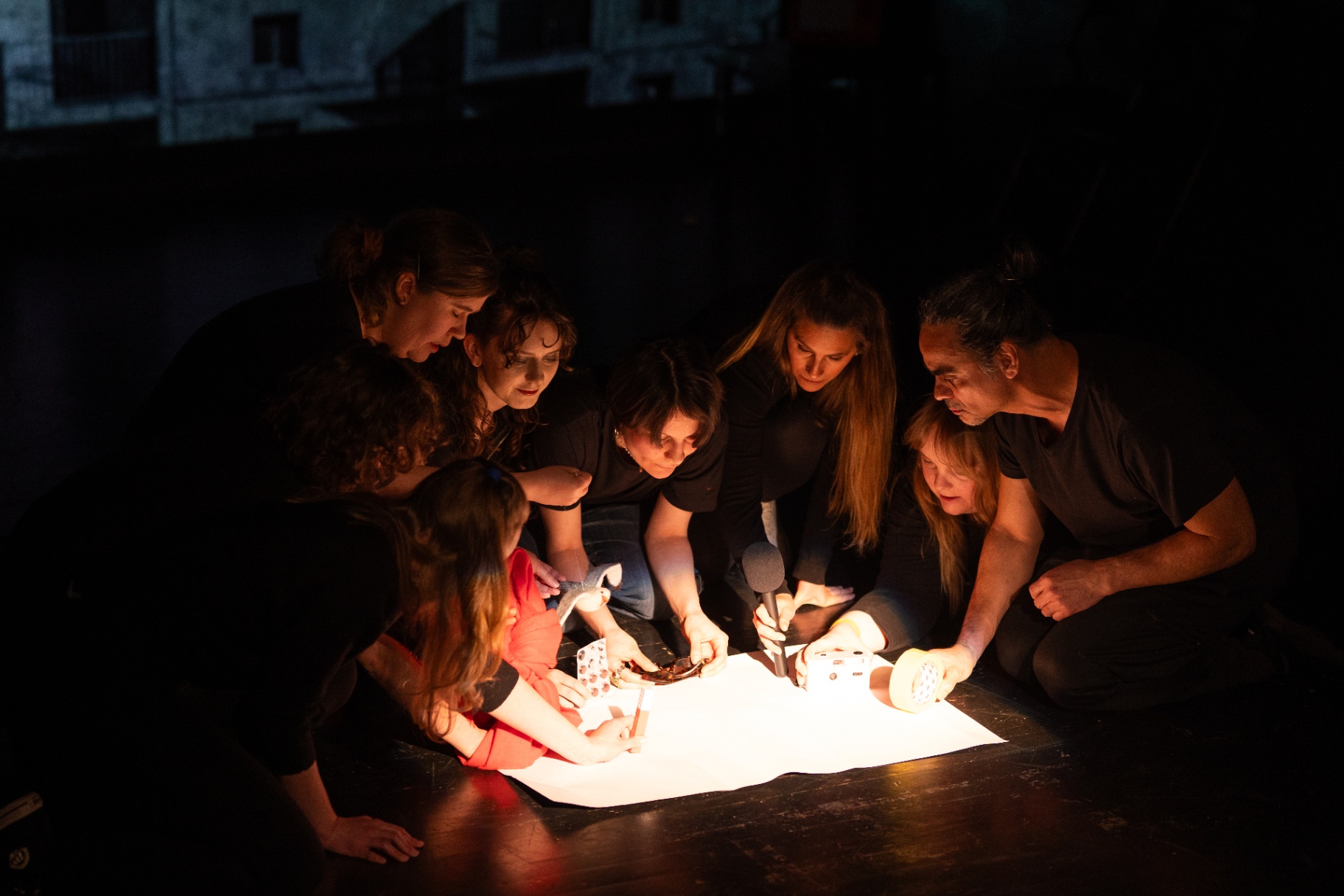 Ensemble gathered around a lit paper on stage