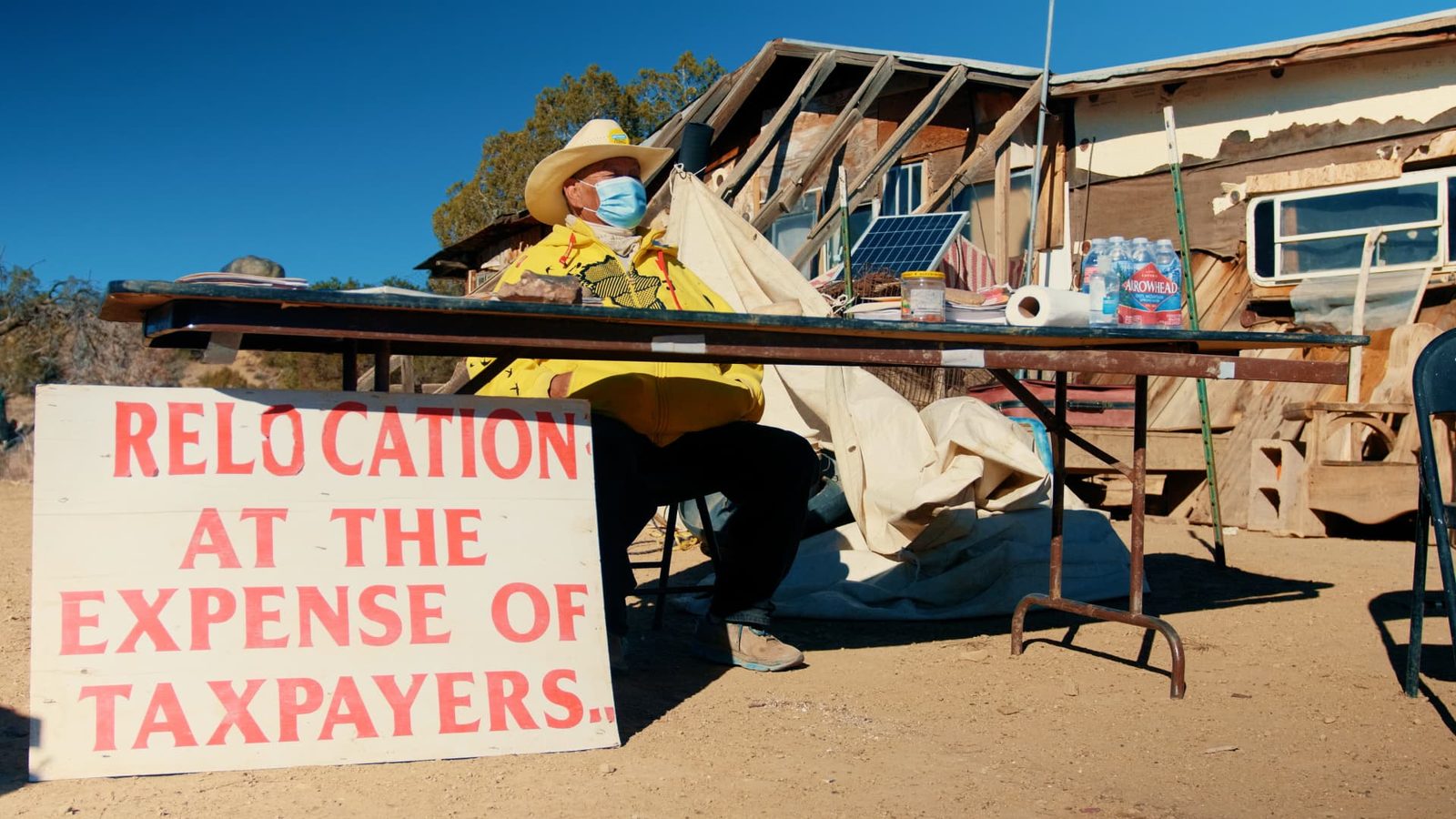 Navajo elder beside a protest sign reading Relocation at the expense of taxpayers
