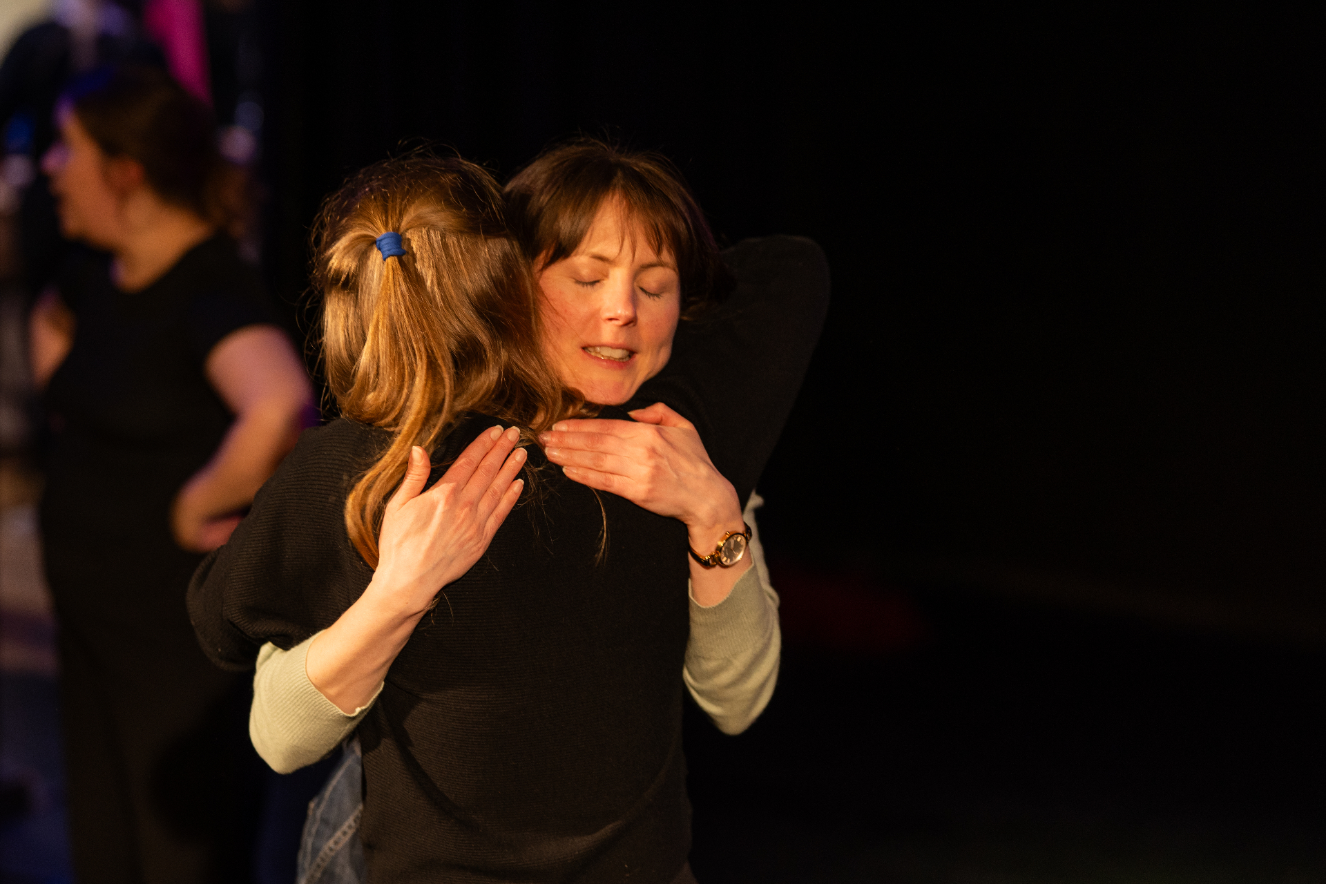 Two performers sharing an embrace on stage in warm light