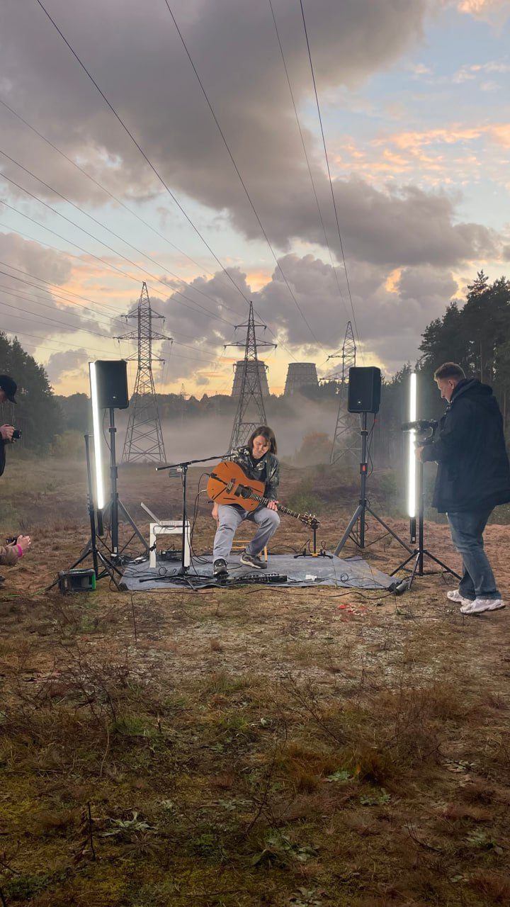 Musician playing guitar at an outdoor session under power lines at sunset